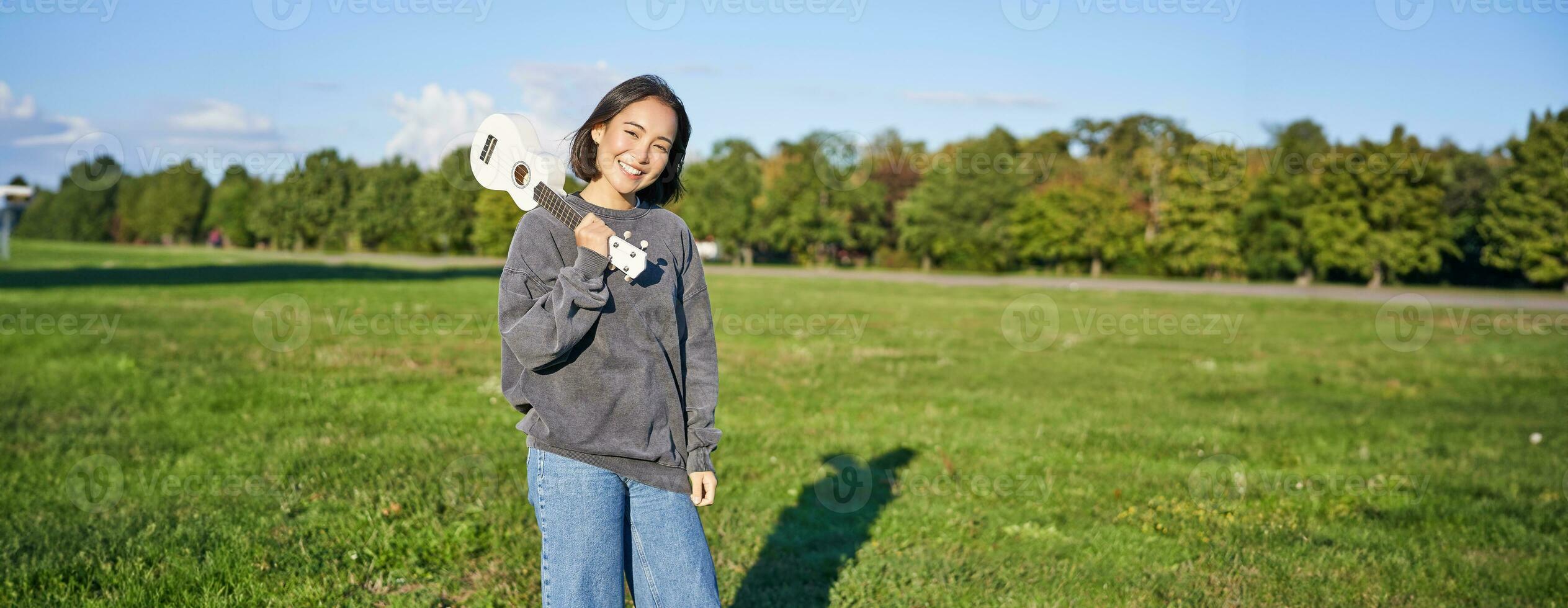 Beautiful korean girl posing with ukulele, young musician playing outdoors in green park on sunny day photo