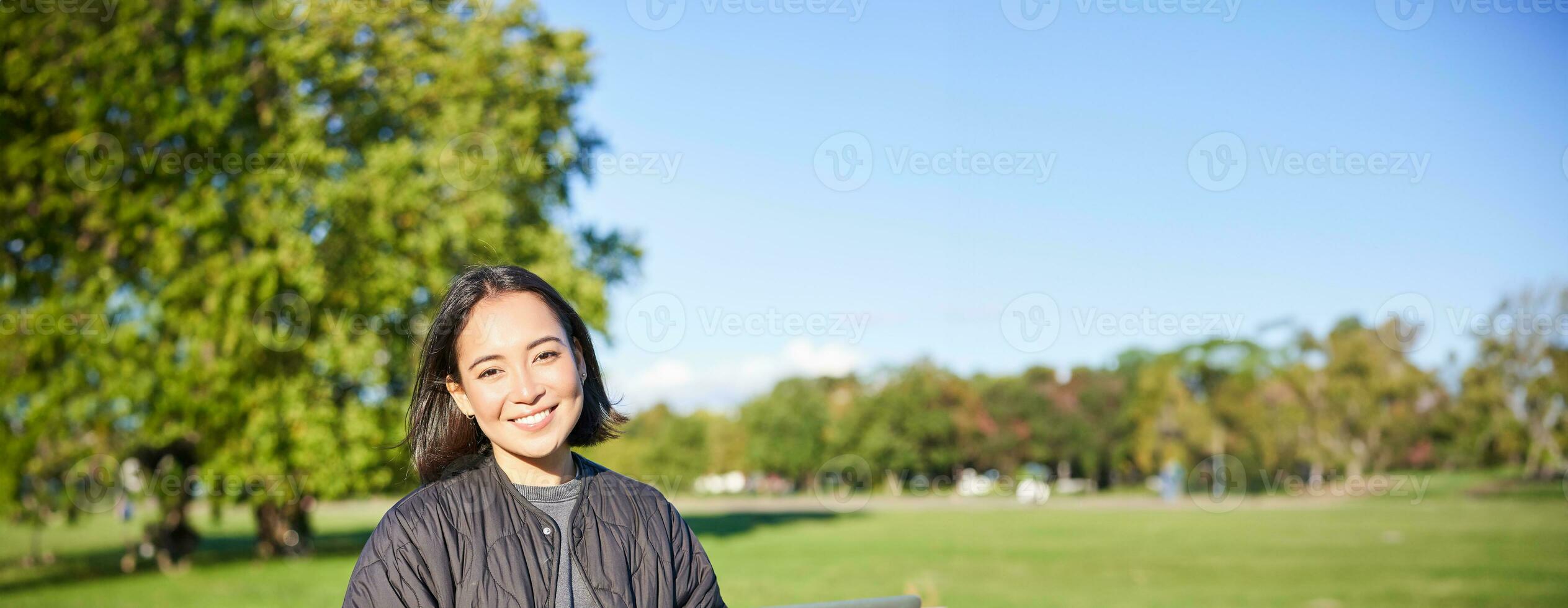 Young asian woman working remotely, freelance girl sits in park with laptop, doing her job from outdoors photo