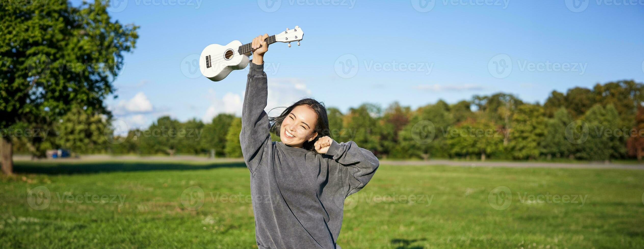 Positive beauty girl with ukulele, dancing and feeling freedom, looking excited, triumphing and celebrating photo