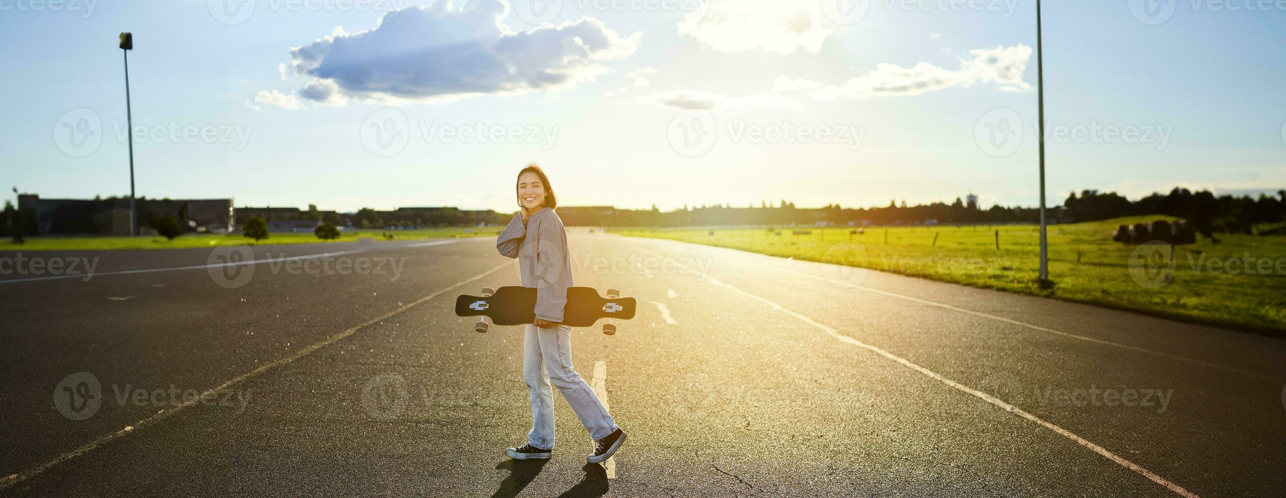 joven patinador chica, adolescente Patinaje en crucero, participación longboard y caminando en hormigón vacío la carretera foto