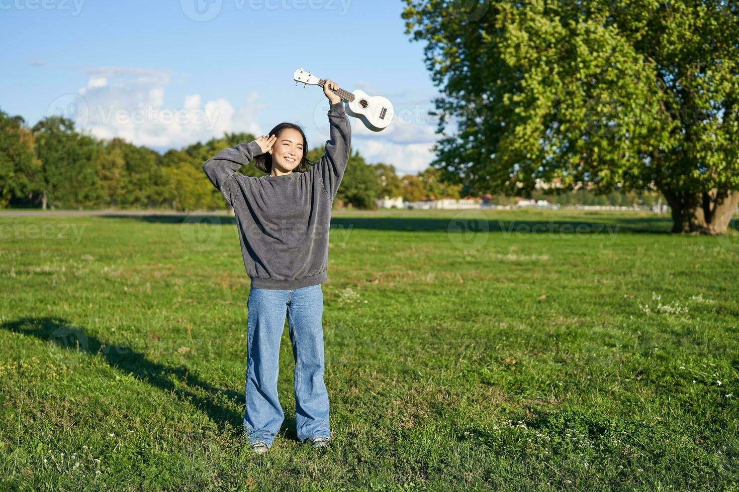 contento asiático chica, músico con ukelele, sensación despreocupado, disfrutando libertad y Fresco aire al aire libre, jugando musical instrumento foto