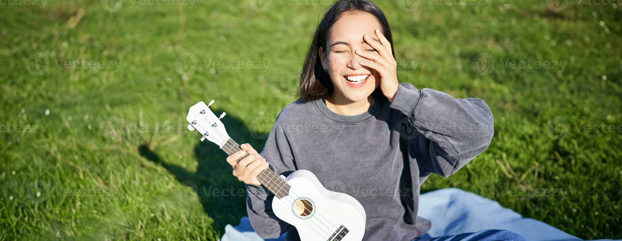 Smiling asian girl with ukulele, playing in park and singing, lifestyle concept photo