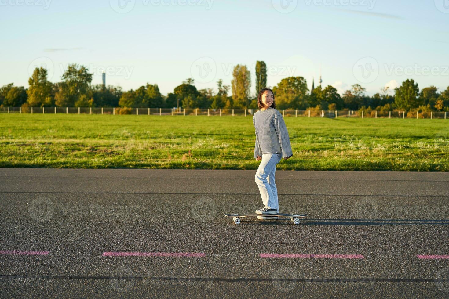 Beautiful asian skater girl riding her longboard on sunny empty road. Young woman enjoying her skate ride smiling and laughing photo