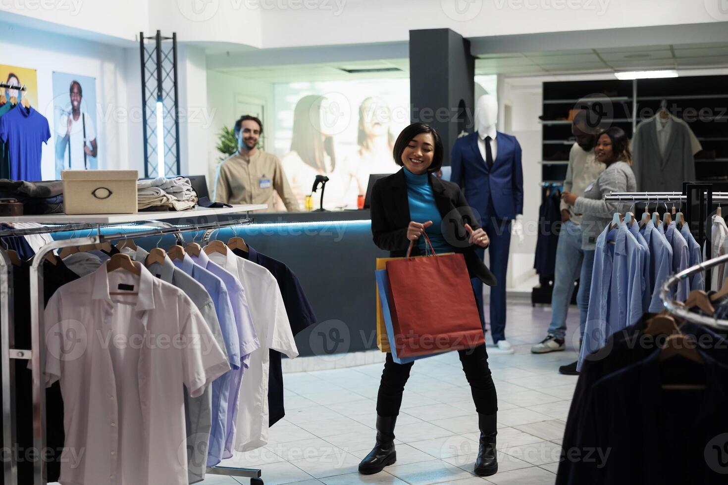 Smiling asian woman dancing with purchases, enjoying buying apparel in clothing store. Boutique cheerful customer holding packages and making moves to music in shopping center photo