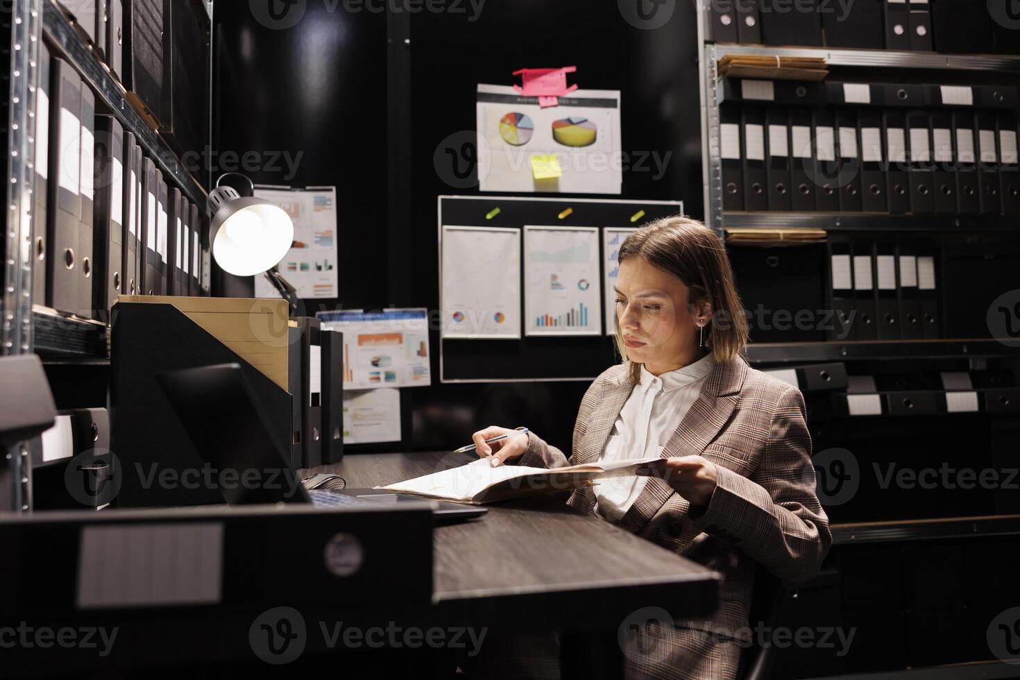 Private detective holding investigations files, analyzing crime scene evidence trying to catch mysterious suspect. Caucasian investigator checking victim report, working late at night in arhive room photo