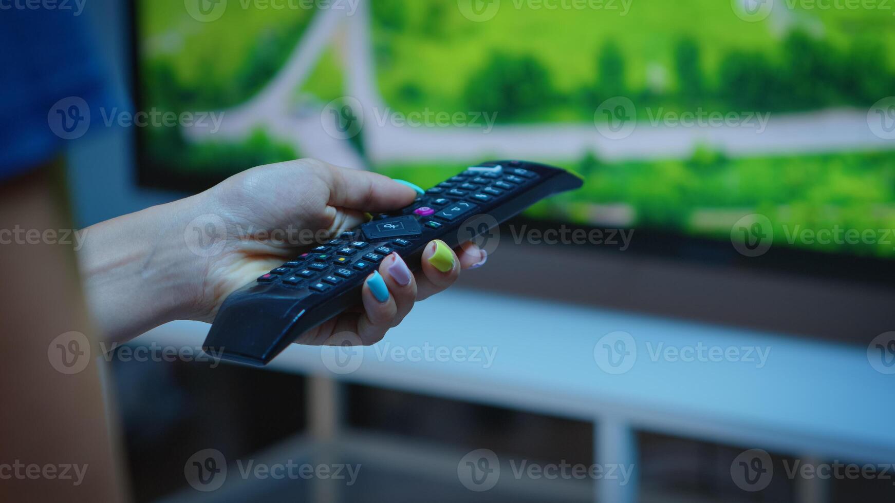 Lady holding TV remote control and pressing the button. Close up of woman hand changing TV channels sitting on comfortable couch in front of television using controller for choosing a movie photo