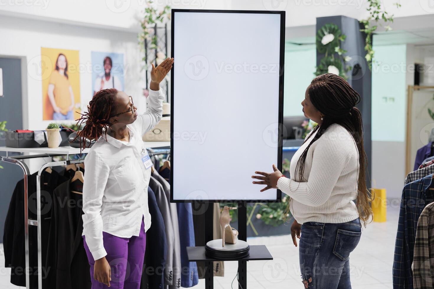 Woman showcasing latest shoe collection to customer on smart display in clothing store. Shopping mall employee using blank whiteboard to assist shopper with selecting trendy stiletto photo