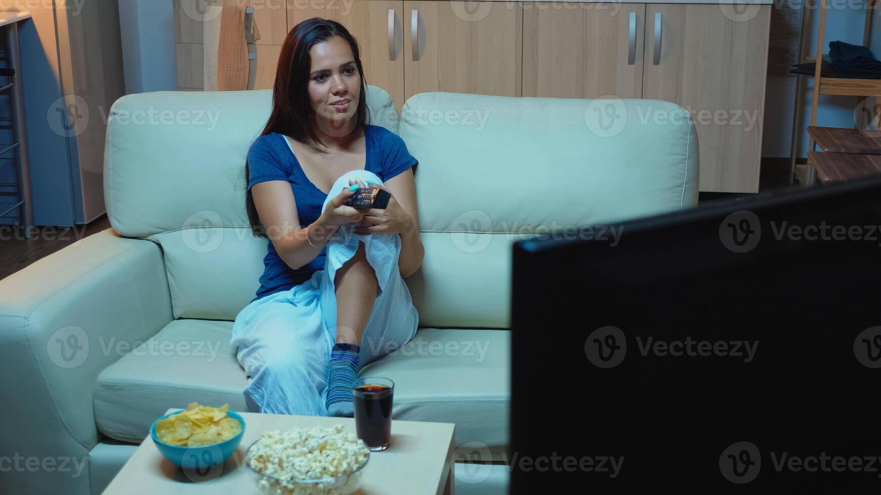 Woman changing Tv channels using remote control. Bored, home alone late at night lady in pijamas relaxing watching tv lying on comfortable couch holding remote control searching a comedy movie. photo