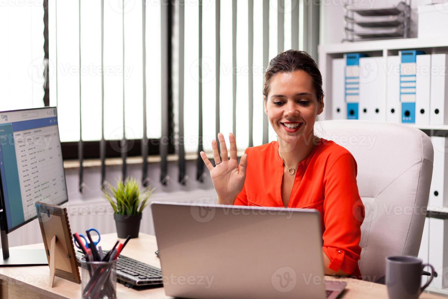 Businesswoman waving at notebook webcam during video conference with coworkers. Entrepreneur using internet connection for video meeting with coworkers looking at webcam. photo