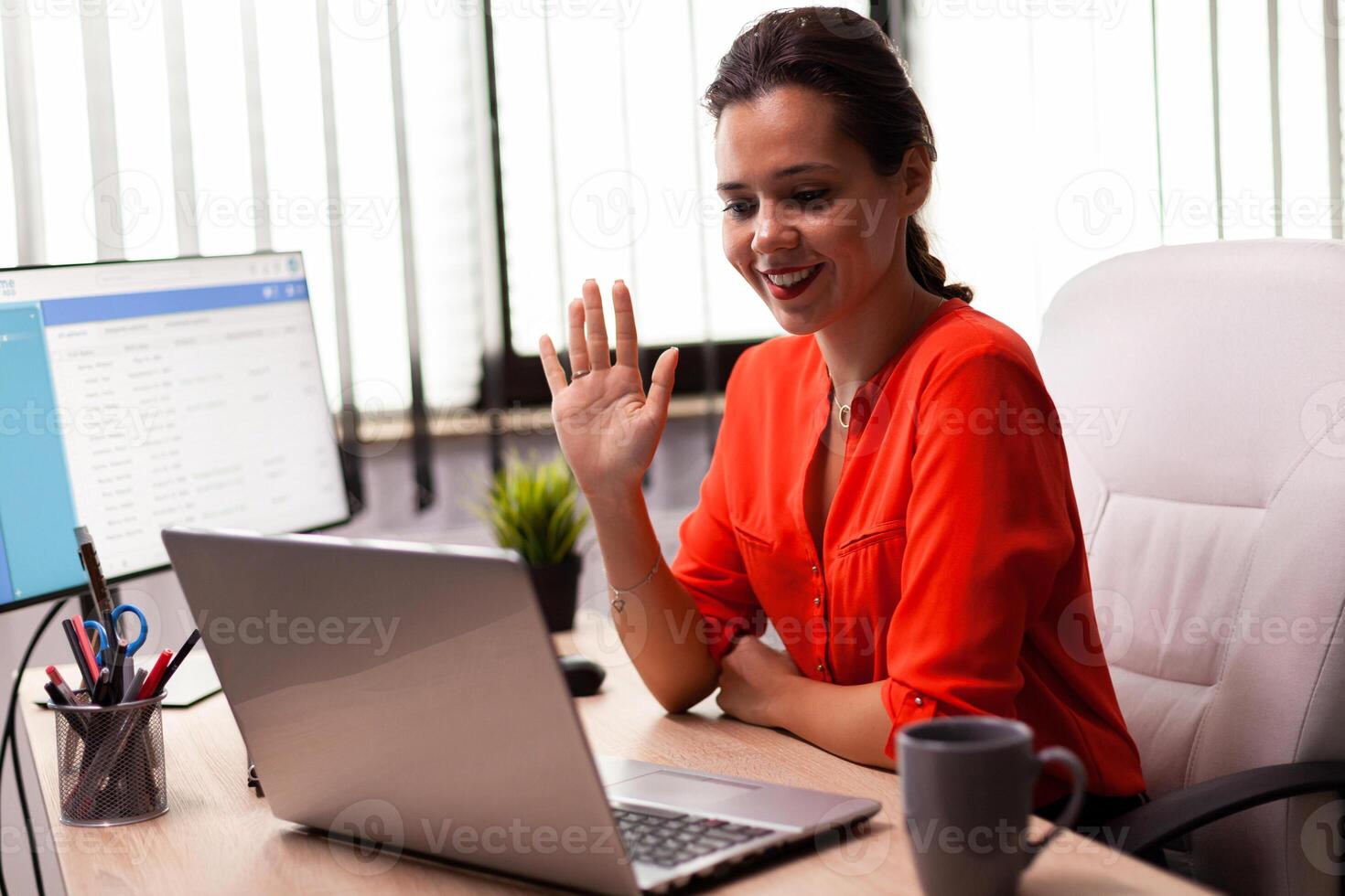 Businesswoman executive in video conference wave at team looking at camera. Entrepreneur using internet connection for video meeting with coworkers looking at webcam. photo