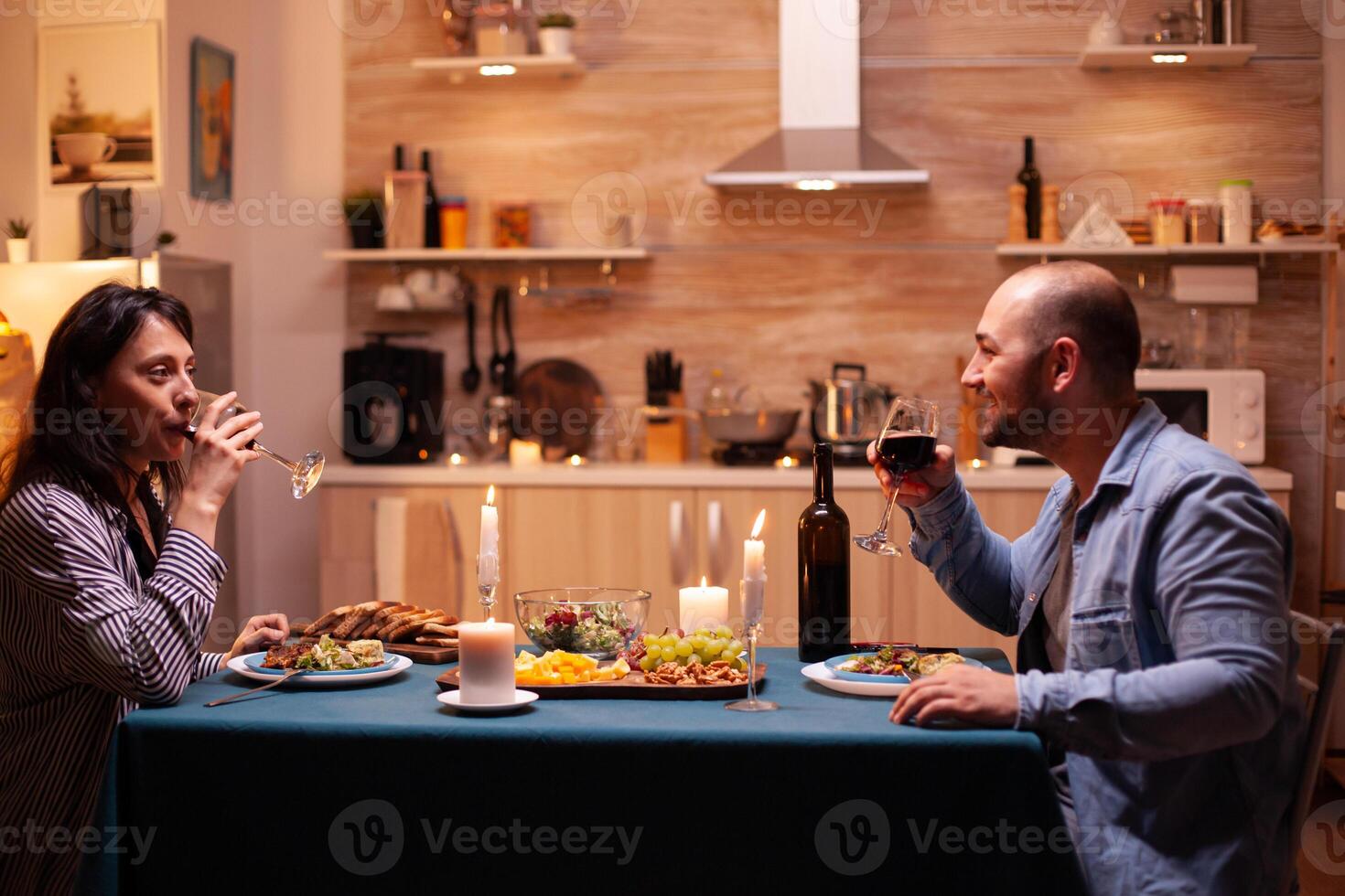 Couple enjoying a glass of wine. Happy couple talking, sitting at table in dining room, enjoying the meal, celebrating their anniversary at home having romantic time. photo