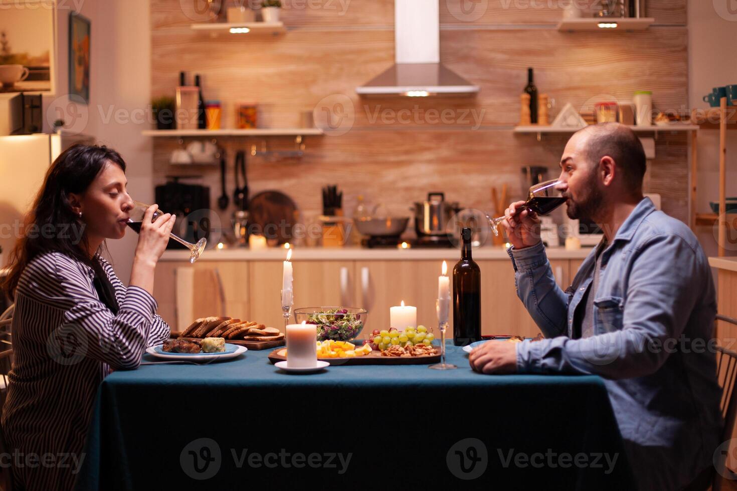 Wife with husband drinking red wine enjoying romantic dinner. Relax happy people ,sitting at table in kitchen, enjoying the meal, celebrating anniversary in the dining room photo