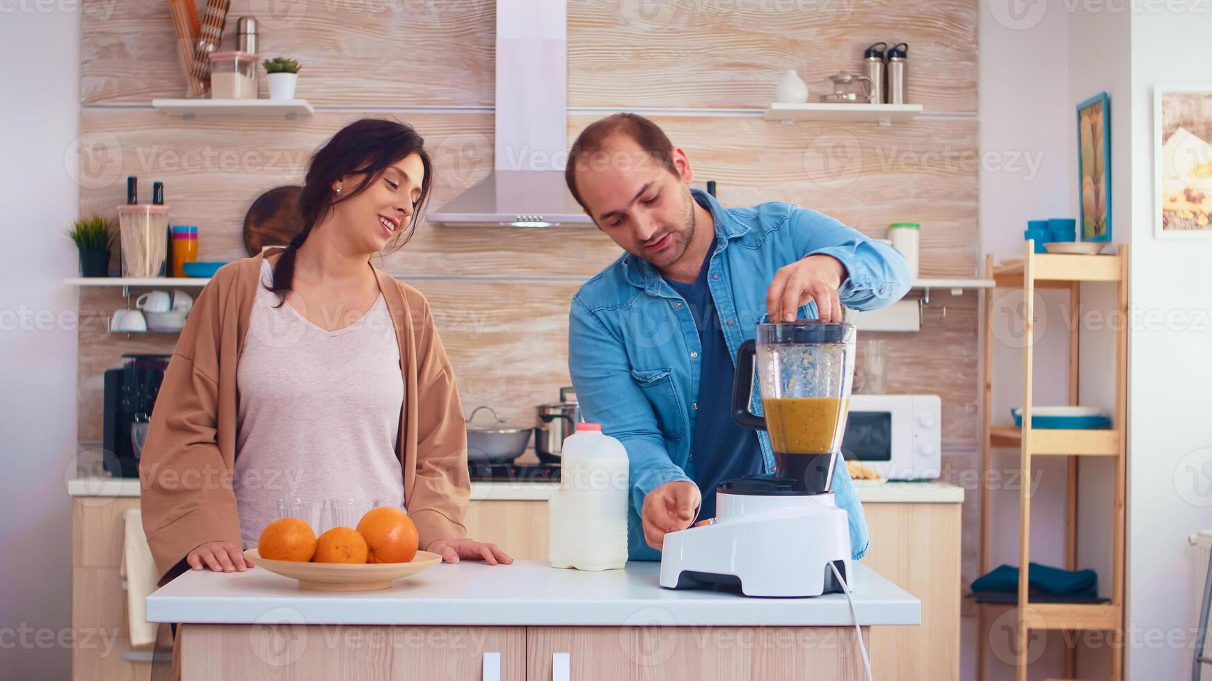 Man pouring milk in blender for fresh and healthy smoothie for him and cheerful wife. Cheerful family making together organic healthy fresh nutritious tasty juice for breakfast from fresh fruits while on a diet. photo