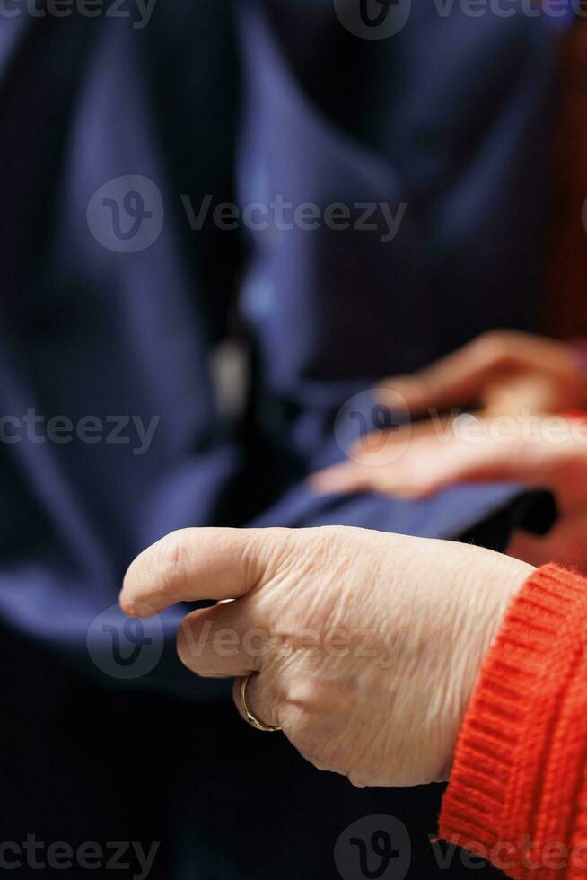 antiguo mujer examinando chaqueta tela antes de comprando ropa a toma de corriente almacenar, cliente haciendo Por supuesto acerca de Derecha Moda elementos. comprador mirando a traje chaqueta de sport presentado por ventas obrero. cerca arriba. foto