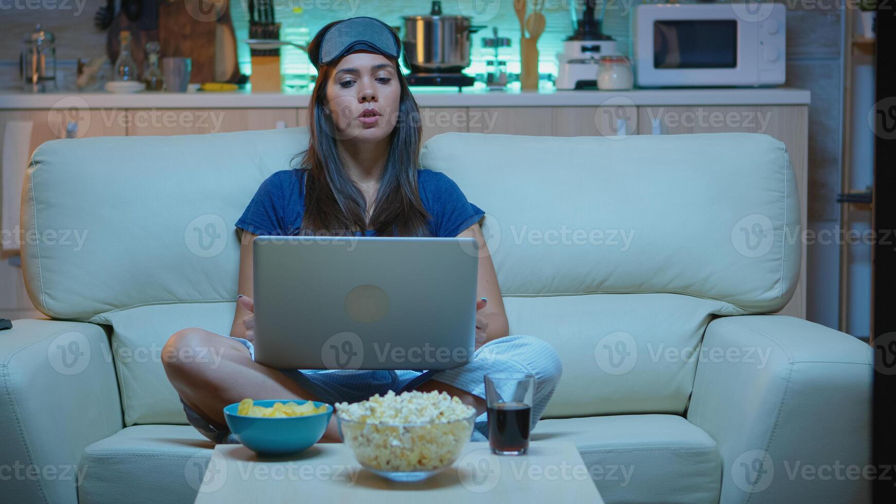 Lady with eye mask having video calling on laptop computer at night. Exhausted person in pijamas talking on notebook computer webcam with colleagues sitting on couch at home using internet technology photo