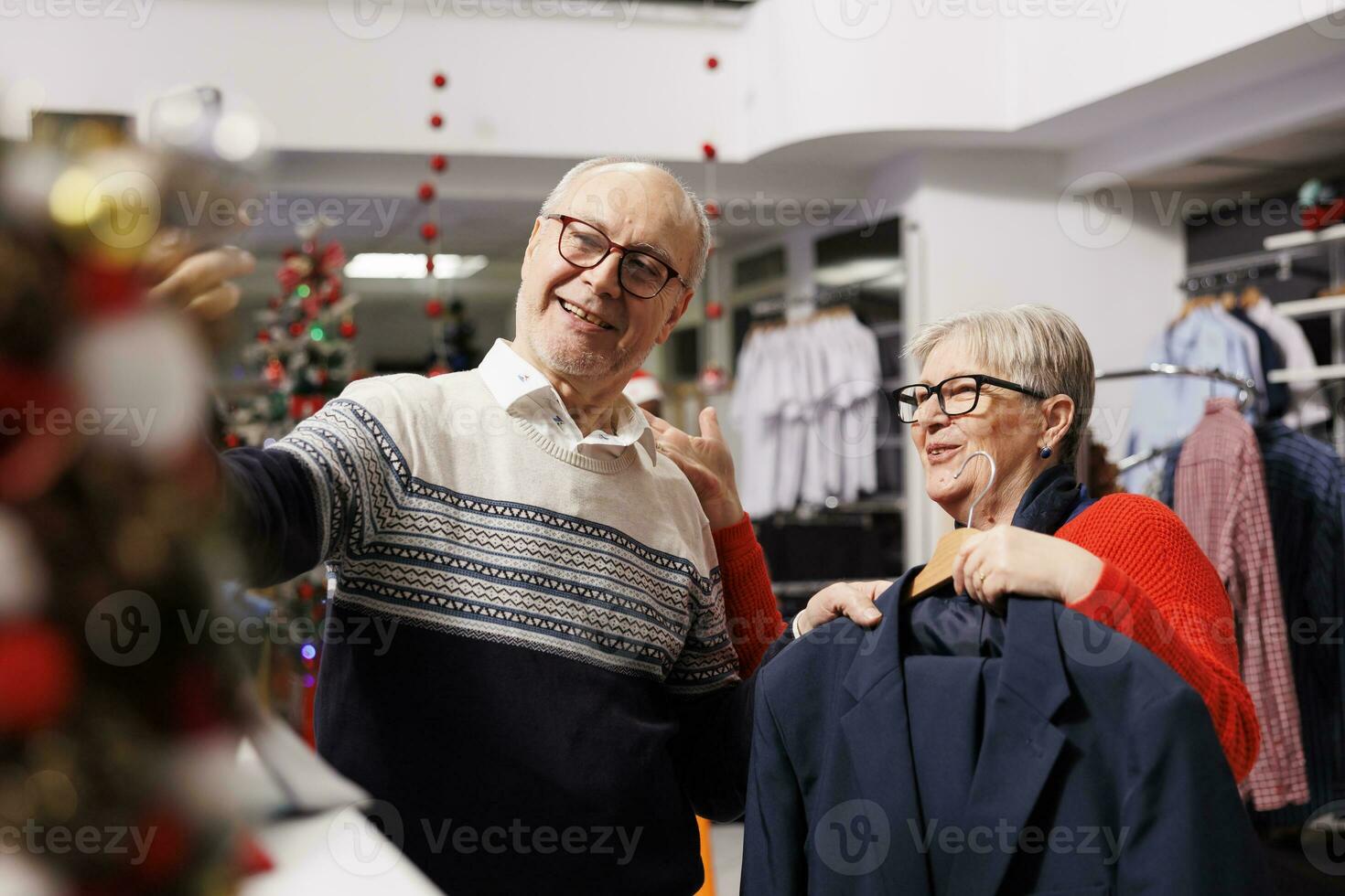 Senior couple searching clothing on videocall in retail store, trying to buy perfect fashion item measurement for christmas festivity. Two older people shopping for xmas gifts during holiday season. photo