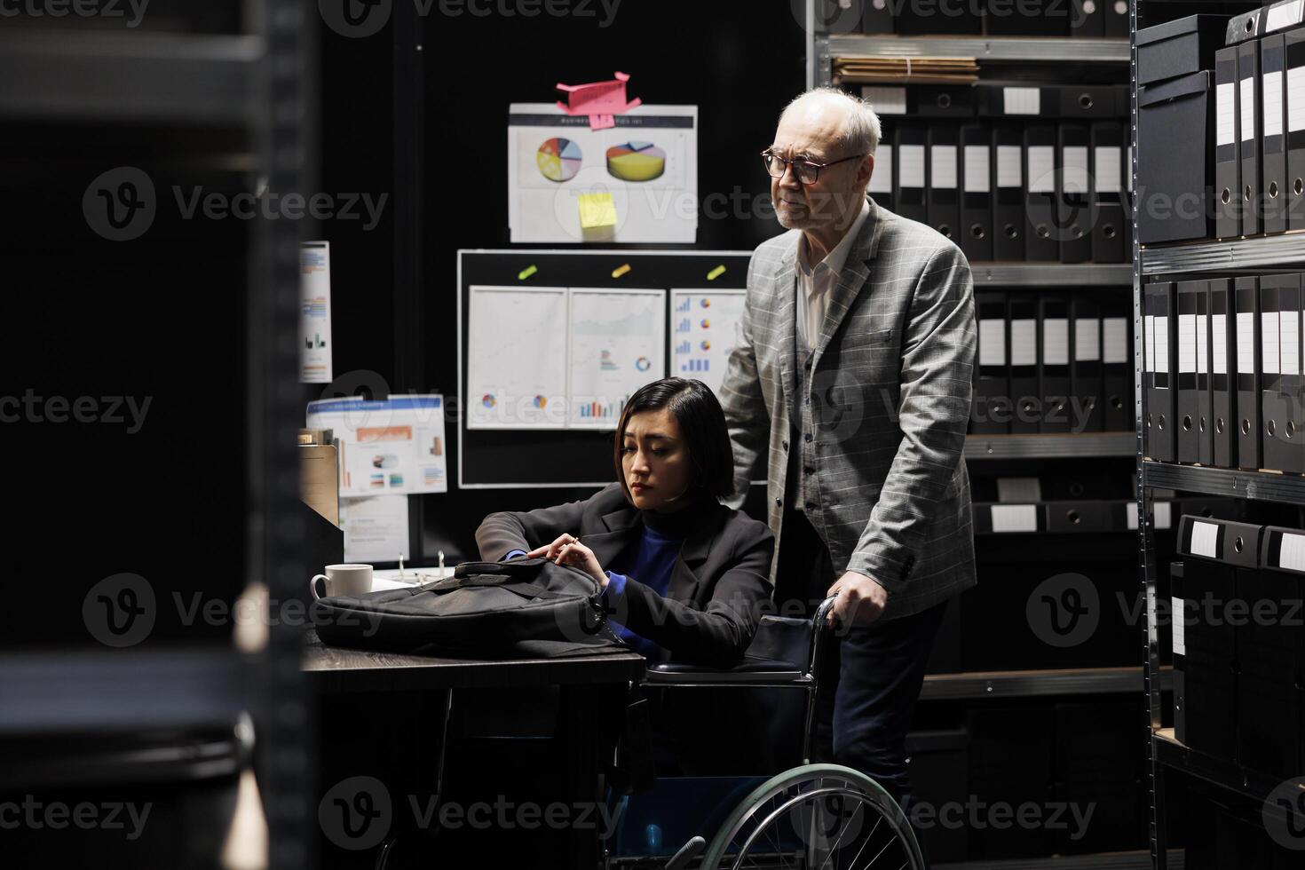 Bookkeeping businesswoman with disability in wheelchair and coworker working in administrative office surrounded by flowcharts. Consultancy bureaucratic workplace filled with business folders photo