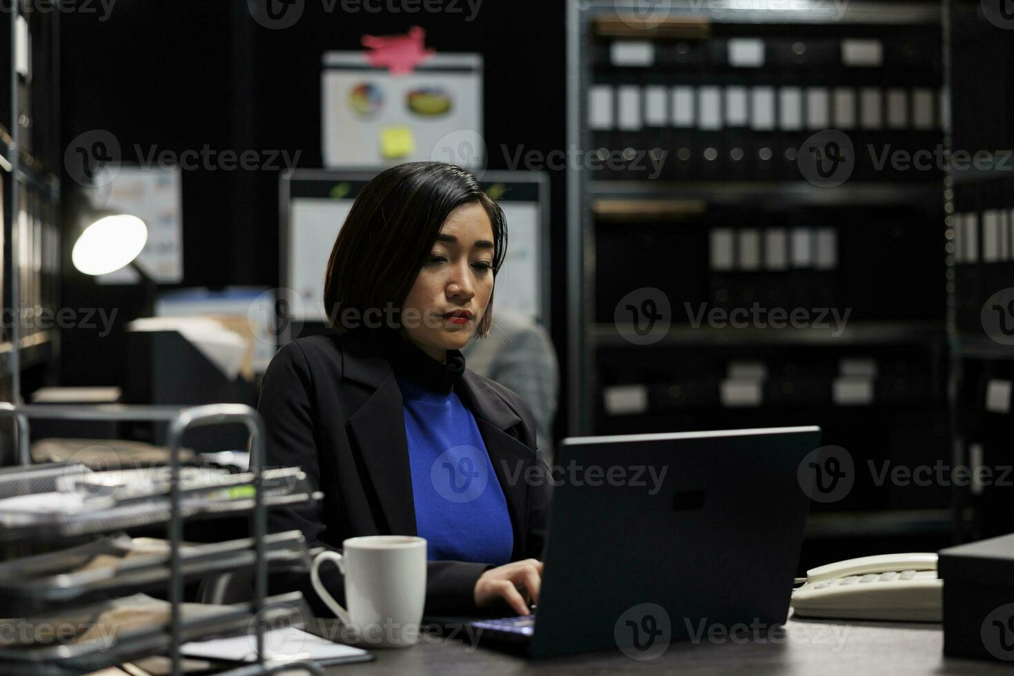 Professional asian accountant checking administrative analytical data on laptop in cabinet office surrounded by accountancy statistic reports. Businesswoman in file storage room photo
