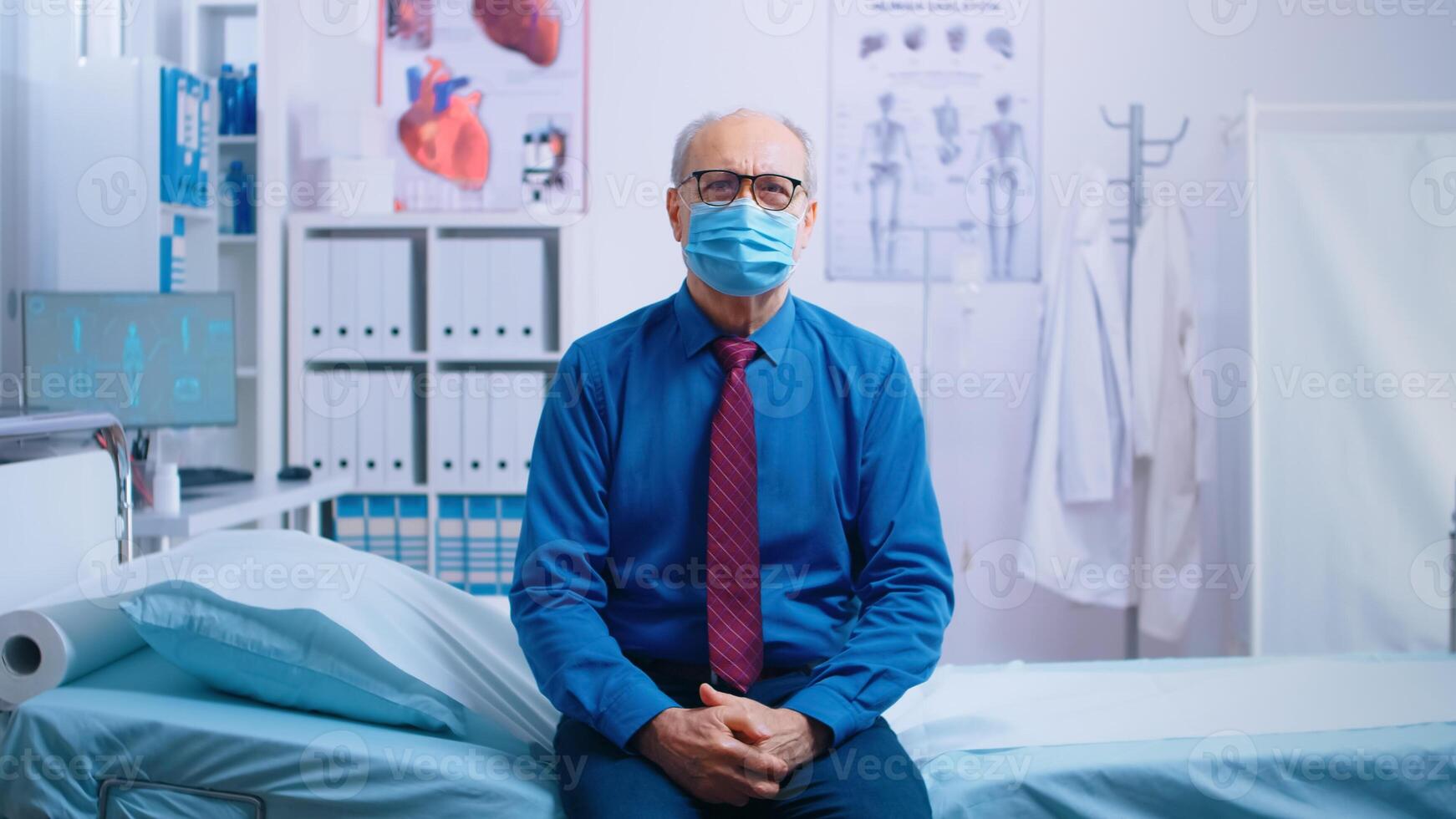 Senior old man waiting for doctor results, sitting on the edge of hospital bed, worring and wearing a mask. COVID-19 medical healthcare consultation, global pandemic. Private modern health clinic photo
