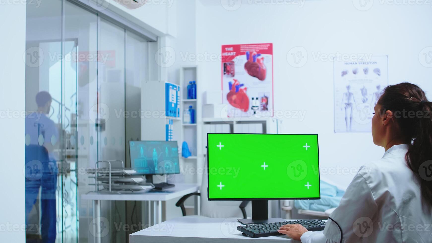 Nurse in blue uniform leaving hospital cabinet and doctor using computer with replaceable display. Computer with repleceable screen used by medicine specialist in hospital and wearing uniform. photo