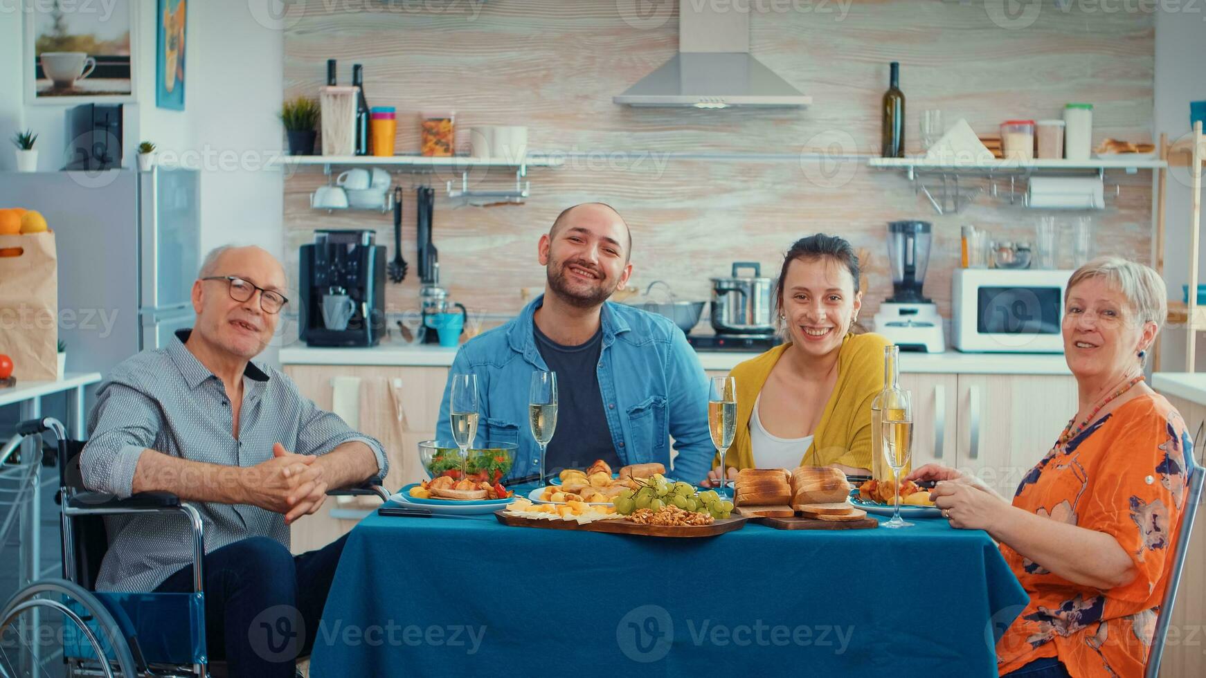 extendido familia y inmovilizado abuelo teniendo un vídeo llamada en su moderno, lujo cocina durante cena. pov en línea Internet moderno, charlando, comunicación, charla conversacion llamada vía cámara web. foto