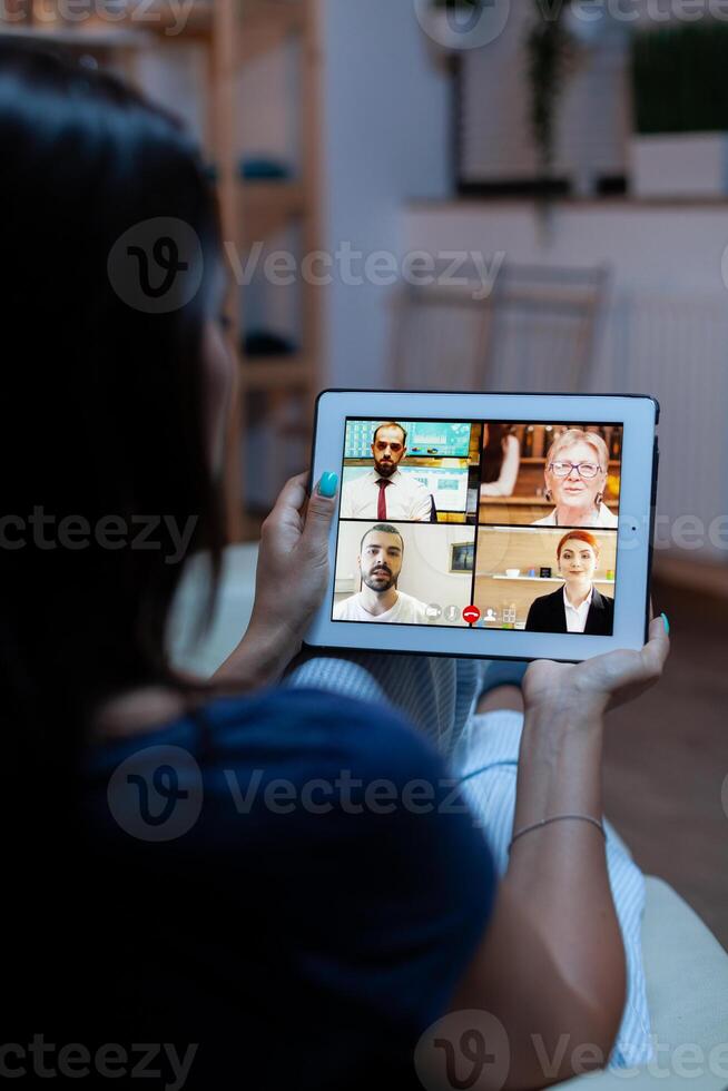 Having online meeting using tablet laying on comfortable sofa at home. Remote worker having online meeting consulting with colleagues on video conference and webcam chat using internet technology. photo