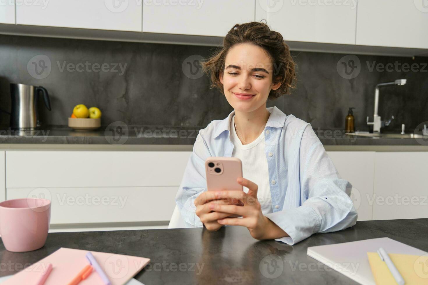 Portrait of beautiful smiling woman sitting at home with smartphone, using mobile phone app, orders groceries delivery photo