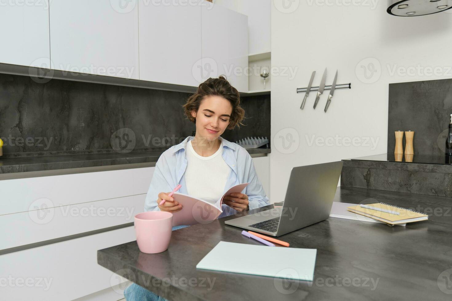 retrato de joven hermosa mujer, estudios a hogar, voltea su libro de trabajo, trabajos desde hogar, usos ordenador portátil a aprender en remoto, hace notas durante seminario web foto