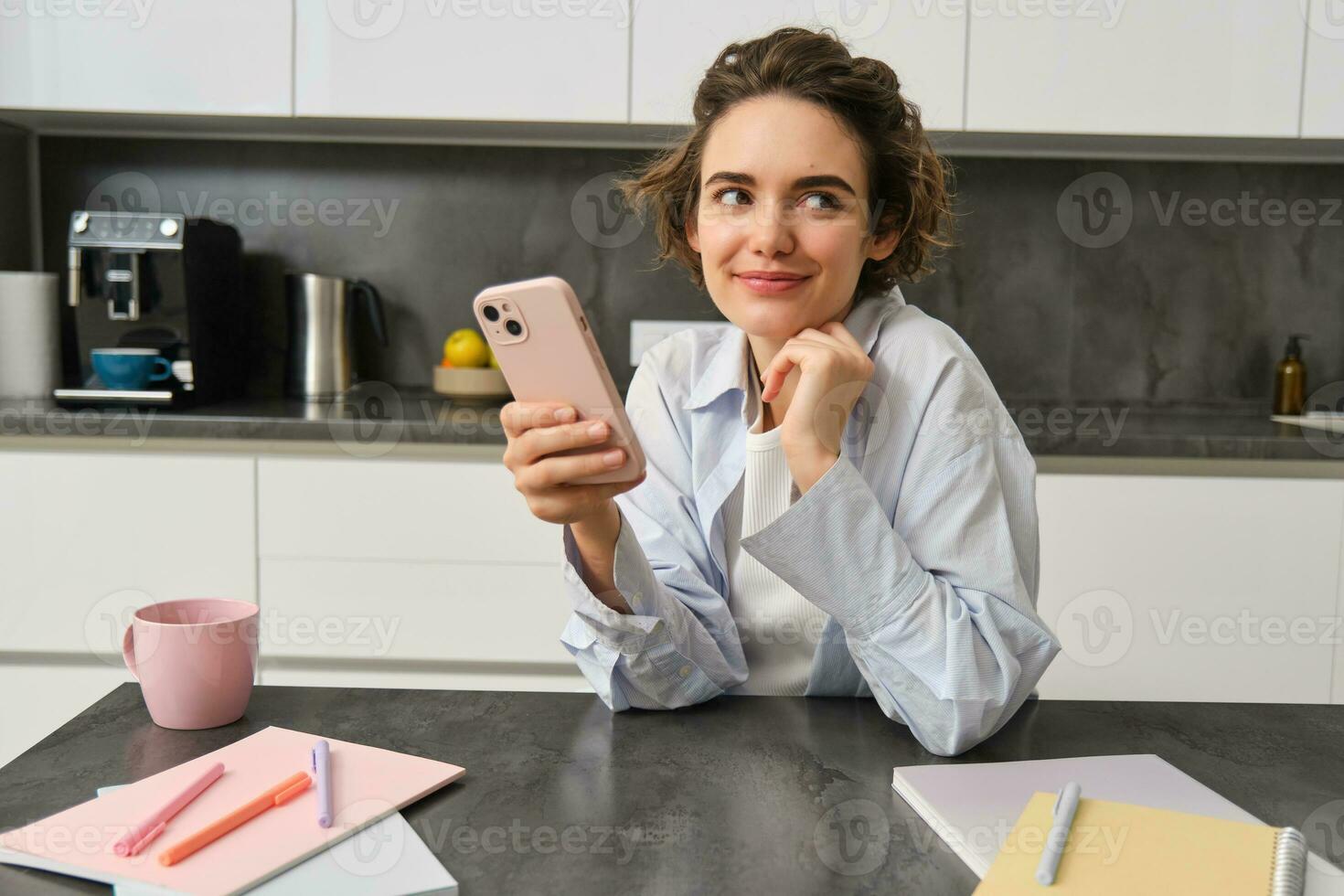 Portrait of beautiful smiling woman sitting at home with smartphone, using mobile phone app, orders groceries delivery photo