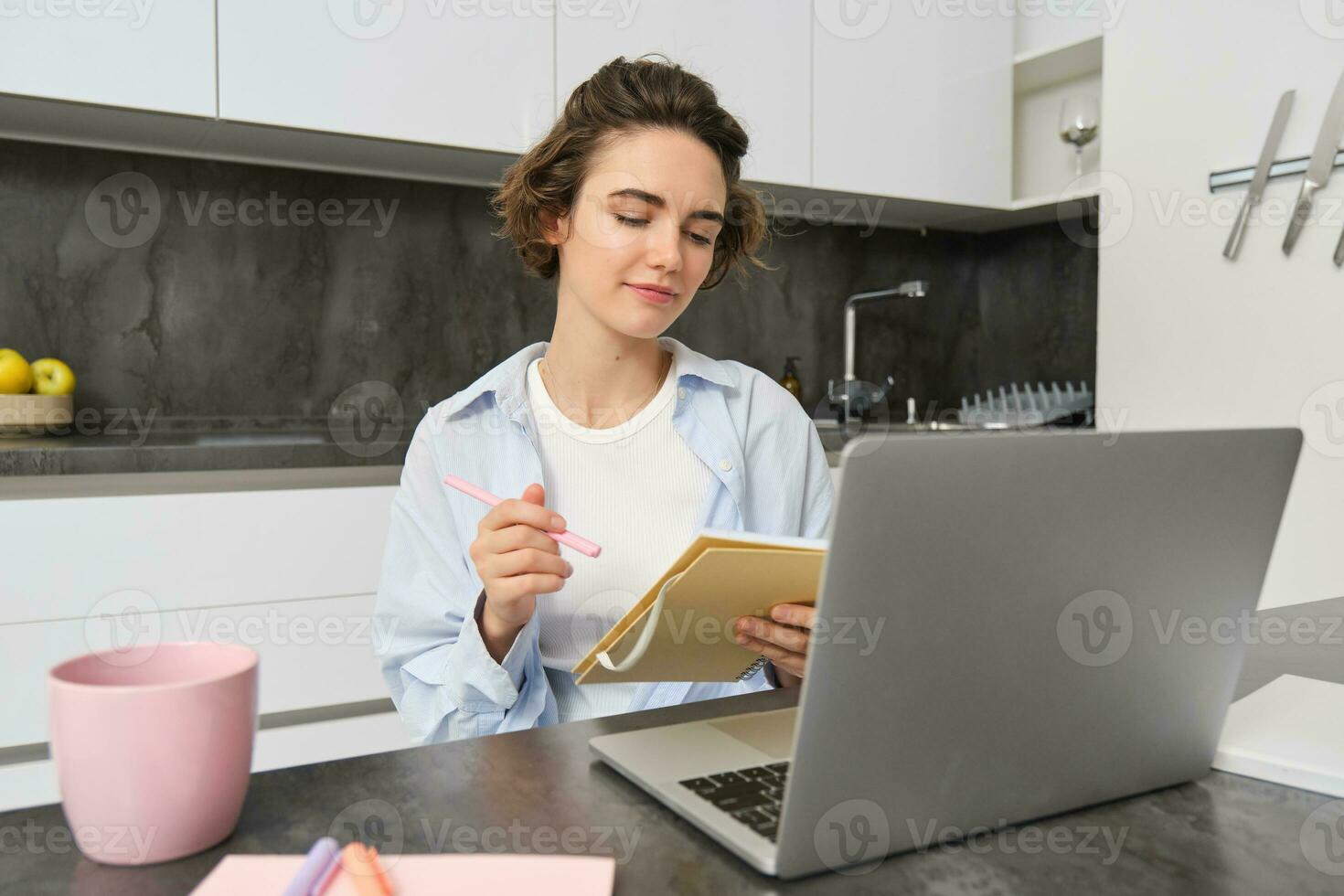 Working woman makes notes, writes down information on notebook, sitting with laptop at home photo