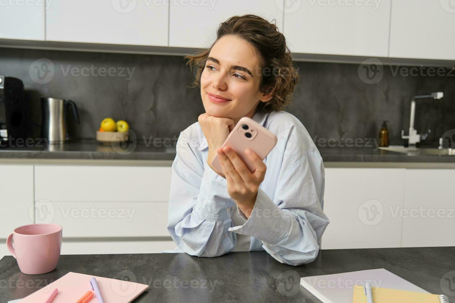 Portrait of beautiful smiling woman sitting at home with smartphone, using mobile phone app, orders groceries delivery photo