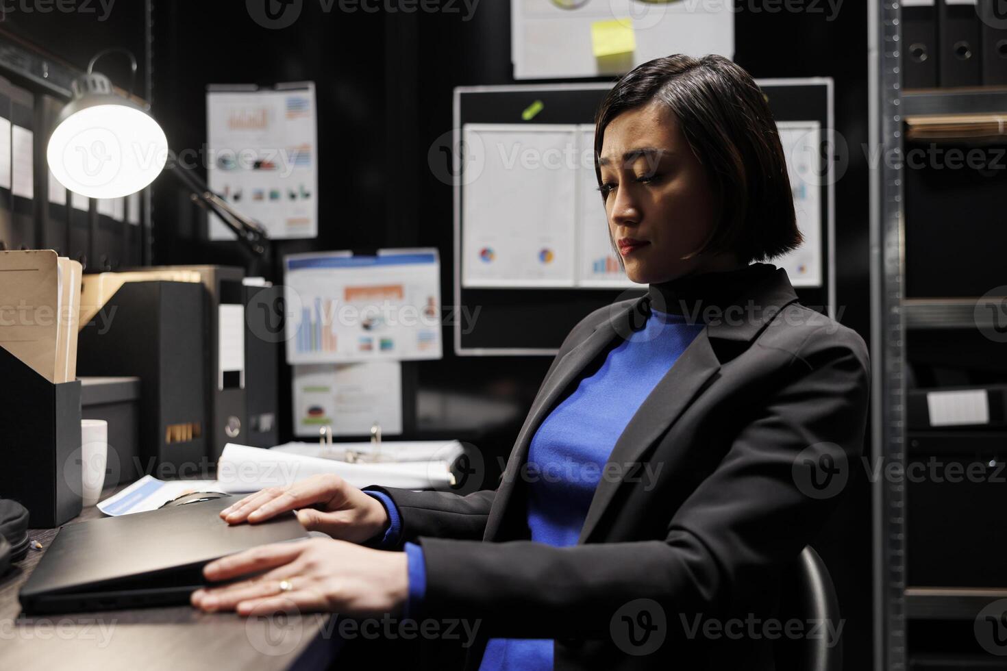 Accountancy asian employee clocking out from work, shutting down laptop in business office. Bookkeeper executive in archival depository filled with cabinet, folders and flowcharts photo