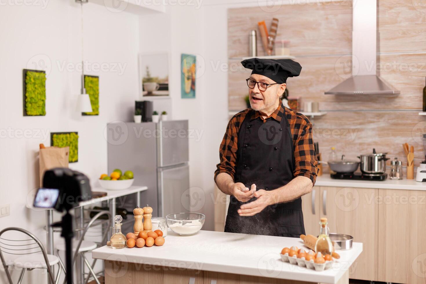 Senior man creating content for culinary blog, explaining the recipe step by step. Retired blogger baker influencer using internet technology communicating, shooting, blogging on social media with digital equipment photo