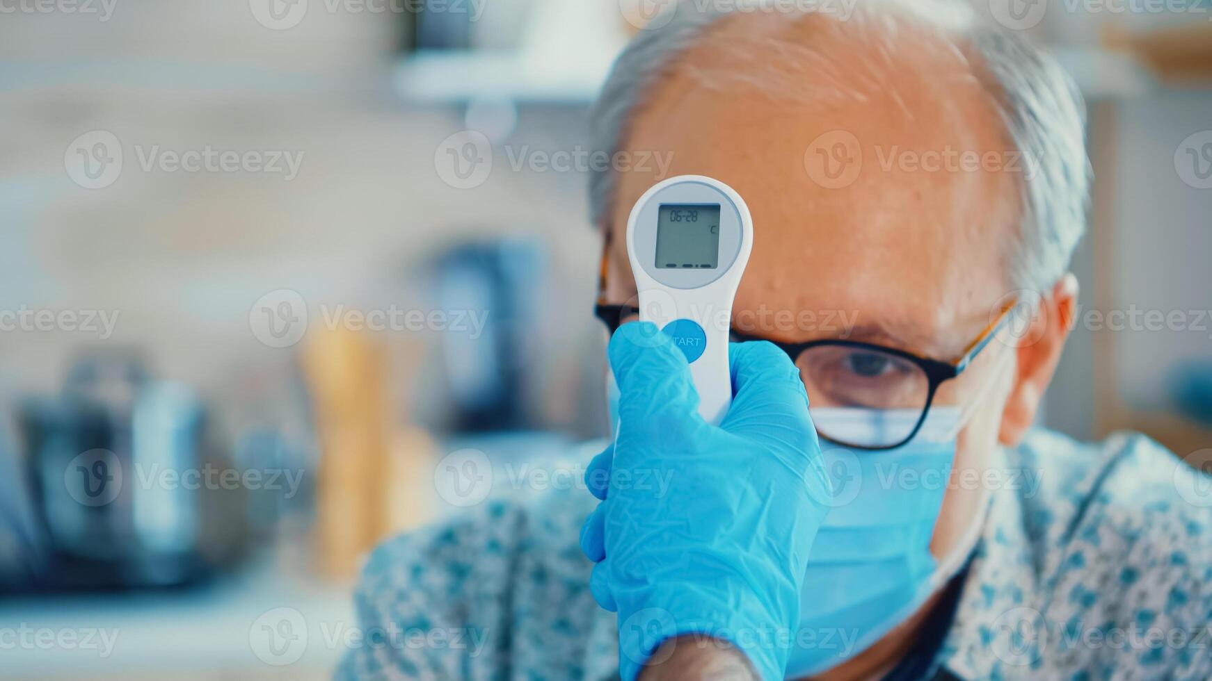 Medical assistance checking senior man body temperature using infrared thermometer in kitchen. Social worker checking on vulnerable persons for disease spreading prevention photo
