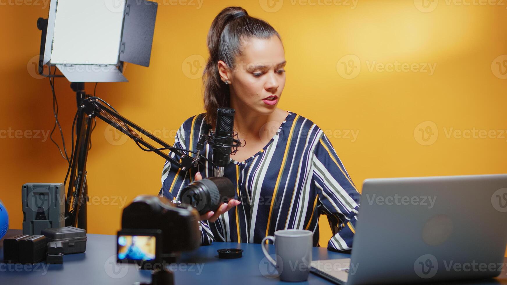 Influencer showing her public a new camera lens and reviewing it in professional studio set. Content creator new media star influencer on social media talking video photo equipment for online internet web show