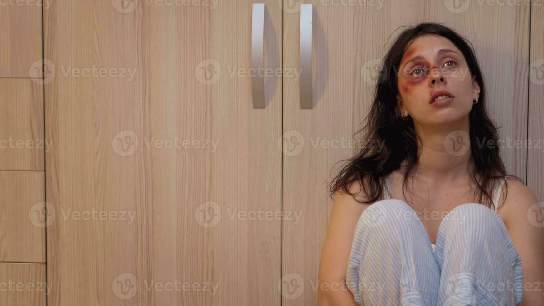 Abused woman sitting on the floor suffering in front of man. Violent aggressive man abusing injuring terrified helpless, vulnerable, afraid, beaten and panicked wife living in terror and pressure. photo