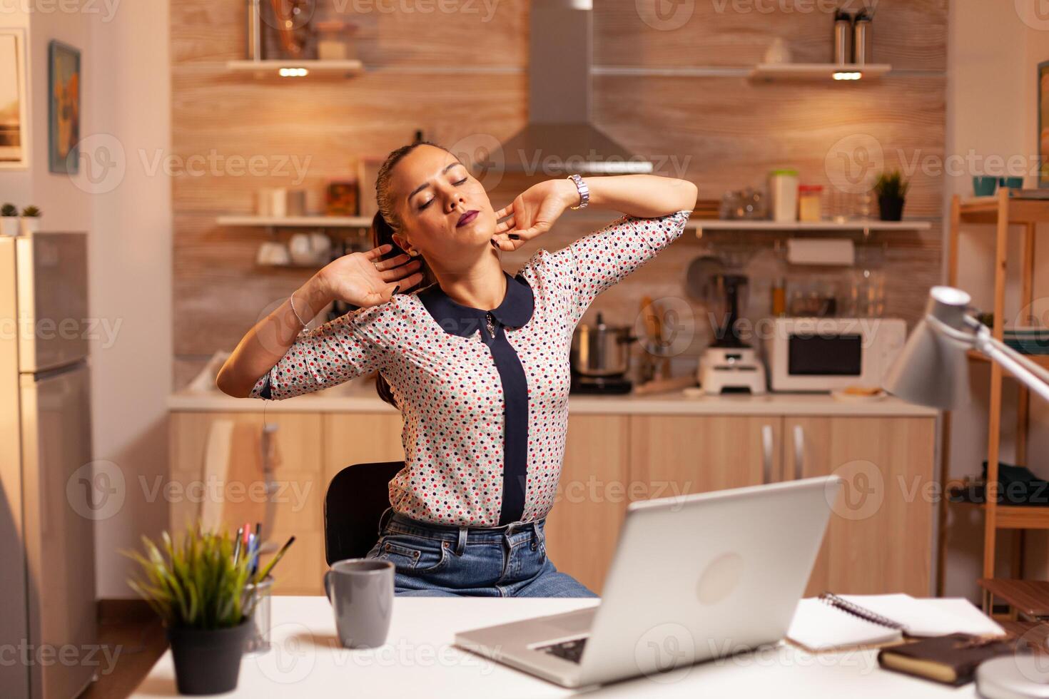 Freelance woman stretching arms because of exhaustion while working overtime from home. Employee using modern technology at midnight doing overtime for job, business, busy, career, network, lifestyle ,wireless. photo