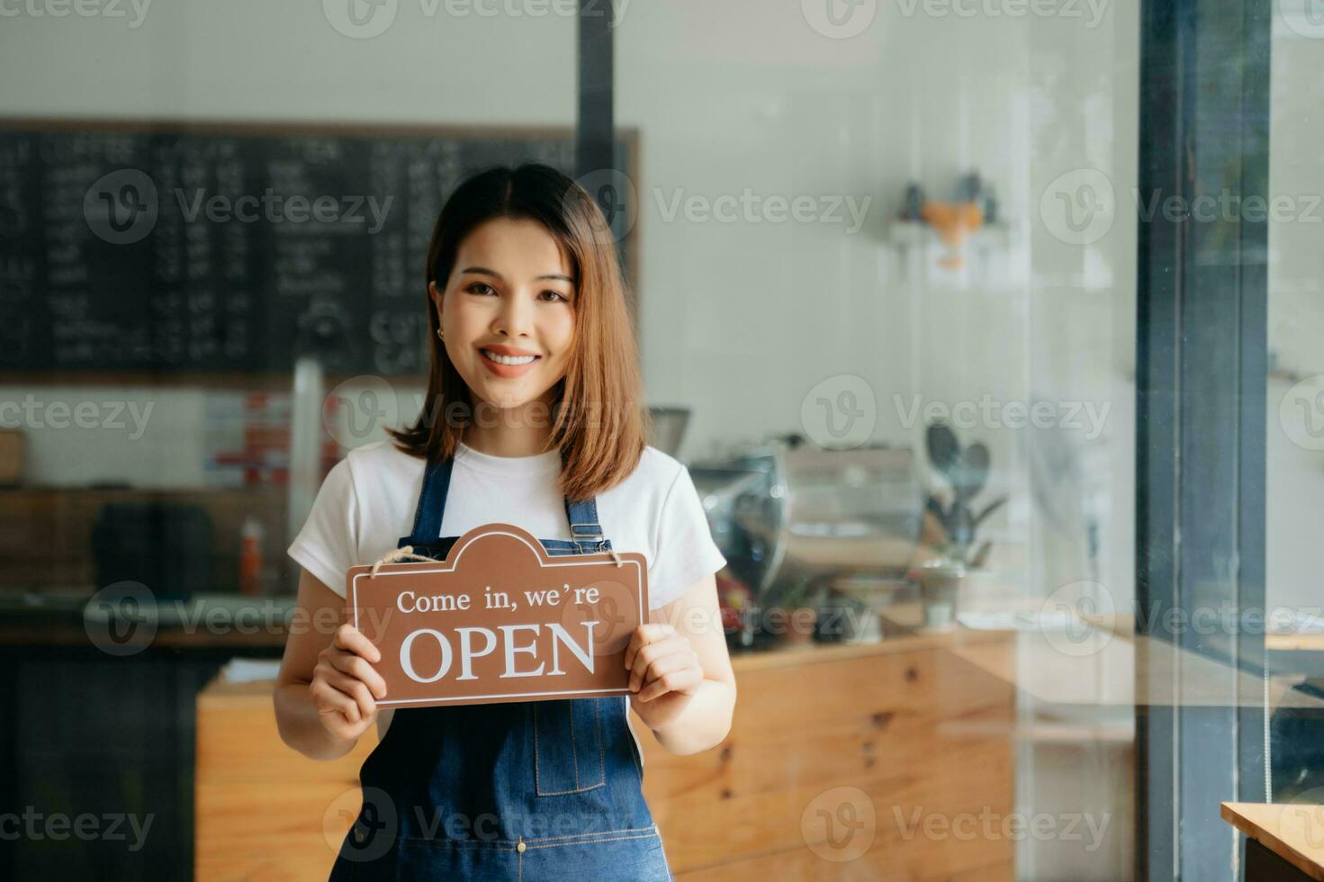 Young female hanging a welcome sign in front of a coffee shop. Beautiful waitress or hostess holding a tablet preparing  in a restaurant. photo