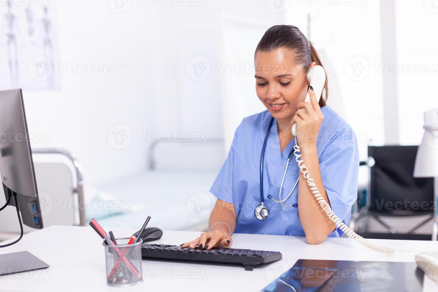 Nurse calling patient from hospital reception to talk about diagnosis. Health care physician sitting at desk using computer in modern clinic looking at monitor. photo