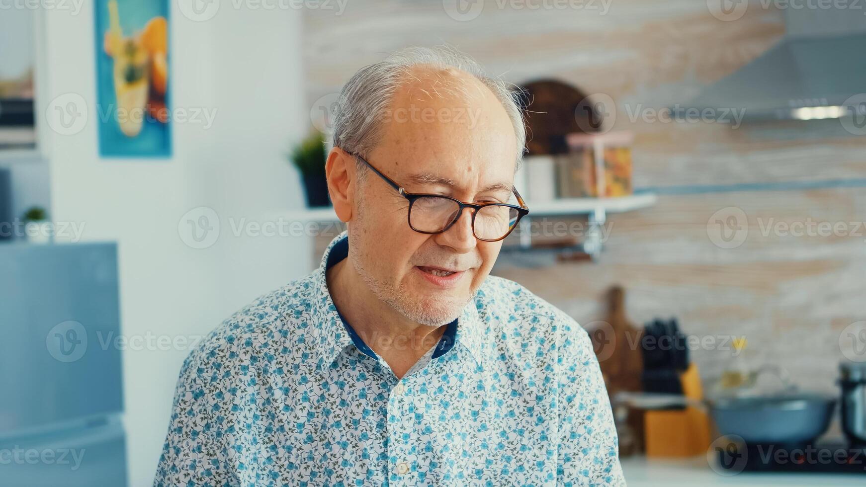Cheerful senior man during video conference in kitchen while enjoying breakfast and a cup of coffee. Elderly person using internet online chat technology video webcam making a video call connection camera communication conference call photo