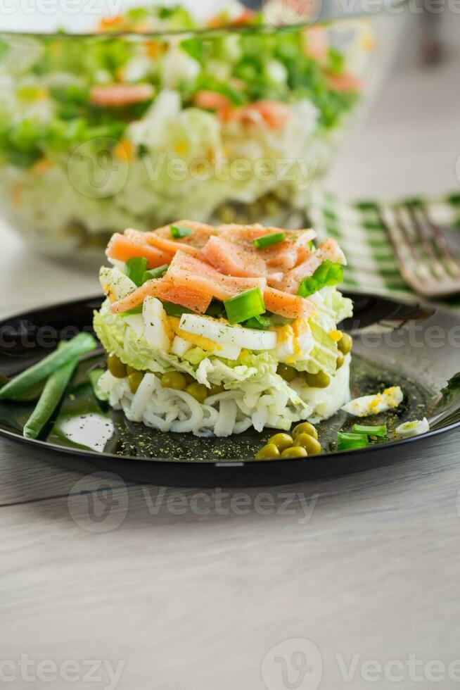 Layered salad of cabbage and other vegetables with pieces of red fish in a plate. photo