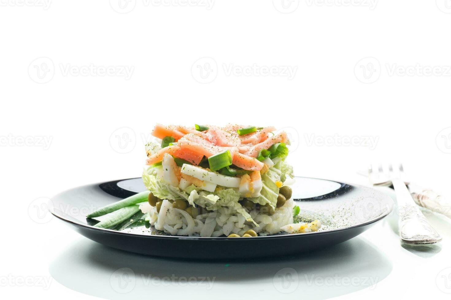 Layered salad of cabbage and other vegetables with pieces of red fish in a plate. photo