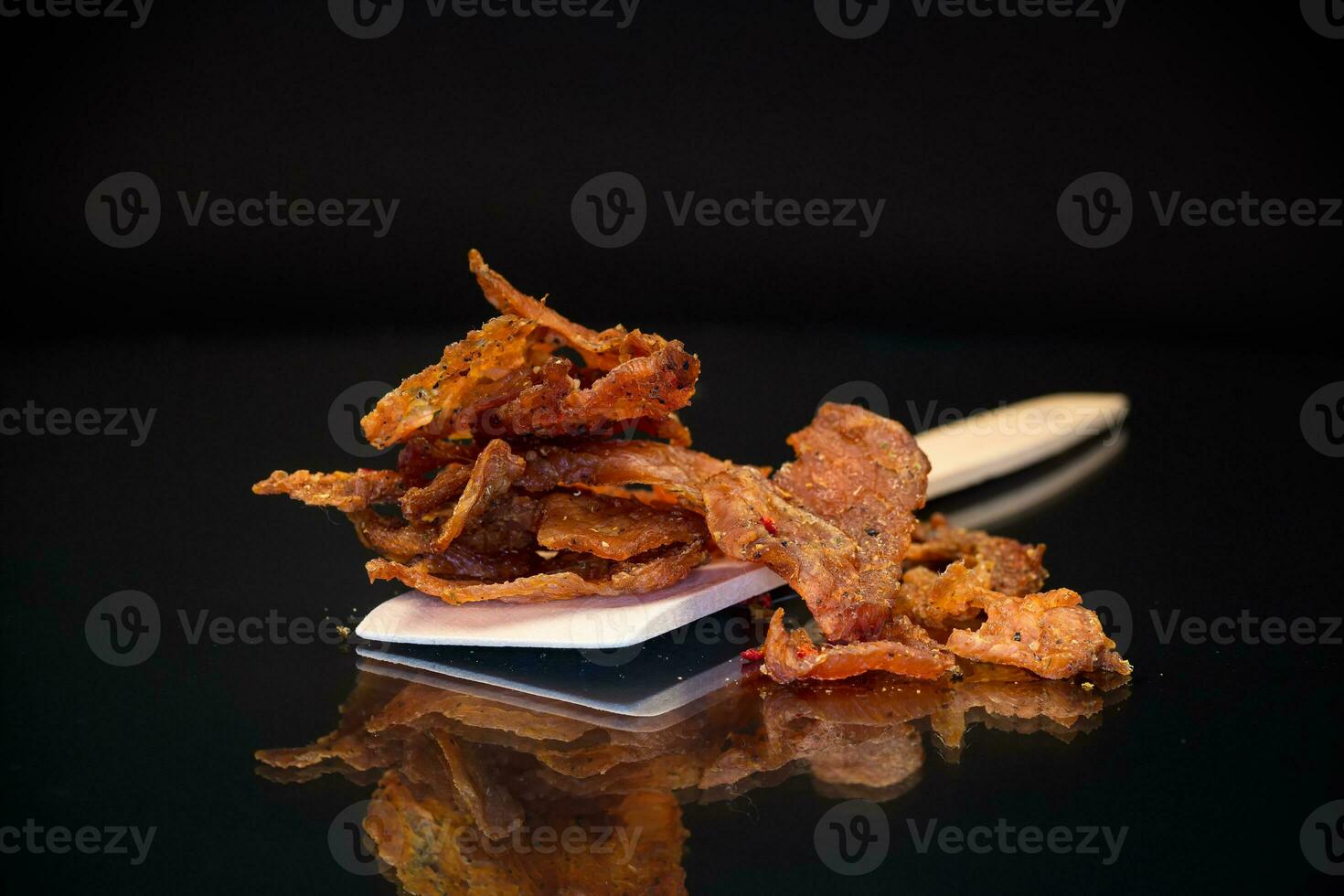 a handful of dried meat marinated with spices on a wooden spoon, isolated on a black background. photo