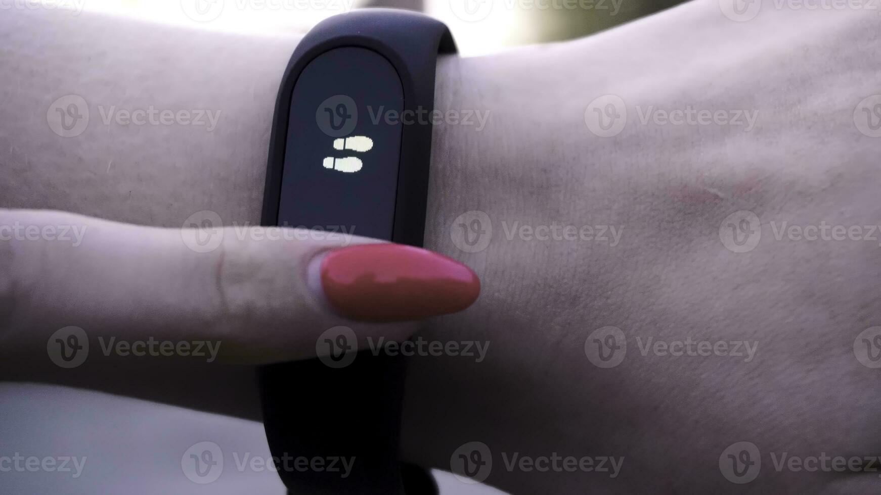 The girls wore a fitness bracelet. Girl checks pulse on fitness bracelet or activity tracker pedometer on wrist, sport, technology and healthy lifestyle concept, close up. Looks at the pedometer photo