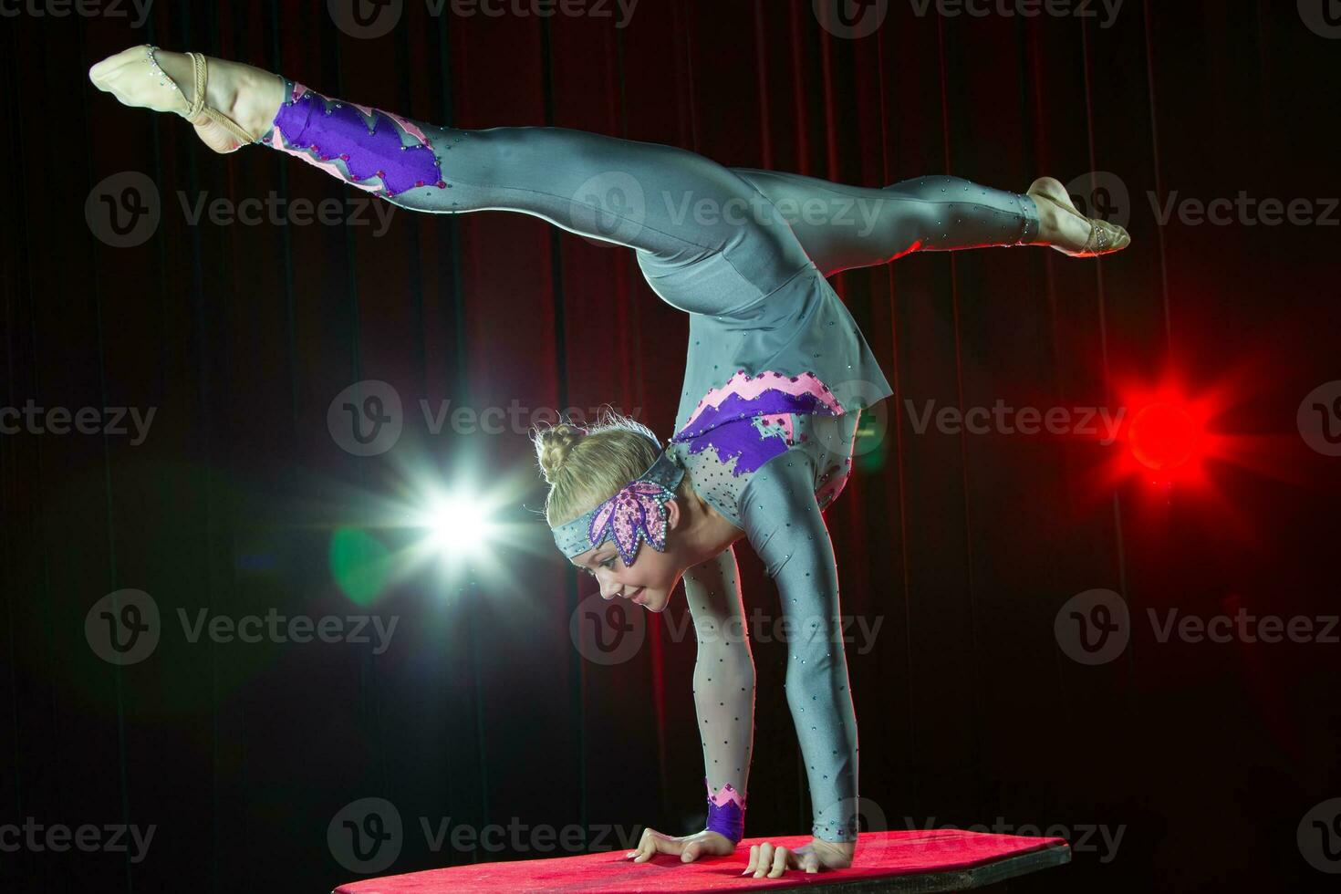 A girl with a flexible body. Performs a circus artist. Circus gymnast. Balancing act. The child performs an acrobatic trick photo