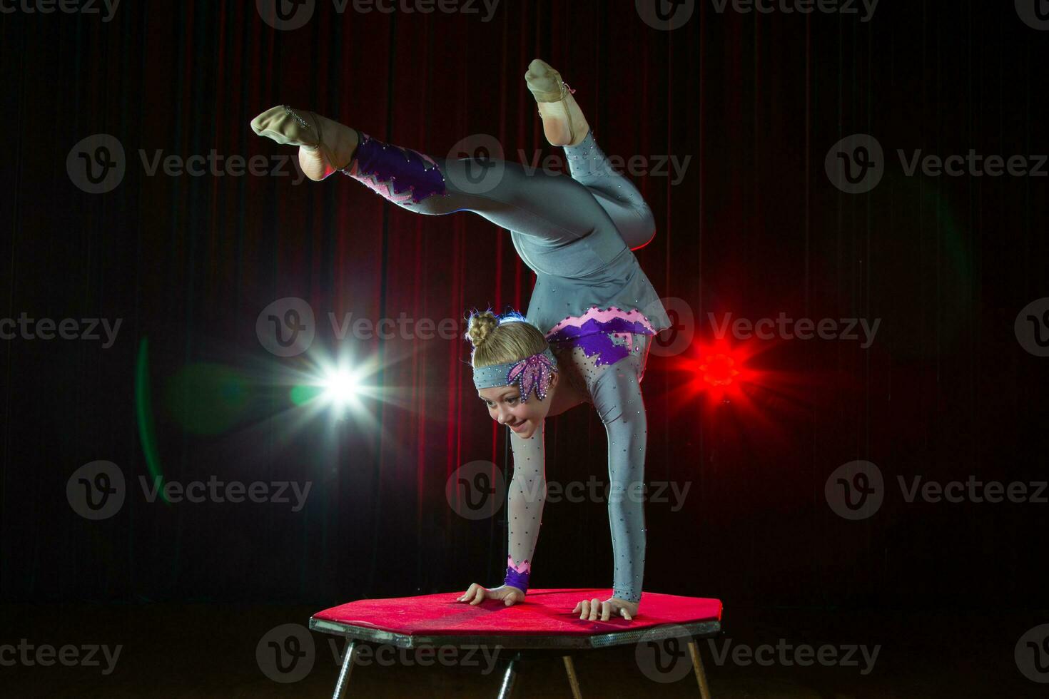 A girl with a flexible body. Performs a circus artist. Circus gymnast. Balancing act. The child performs an acrobatic trick photo