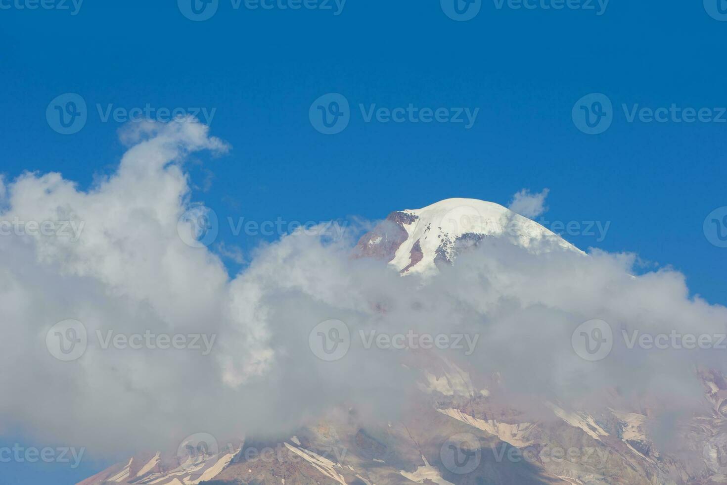 The majestic Mount Kazbeg in flying clouds against the blue sky. photo