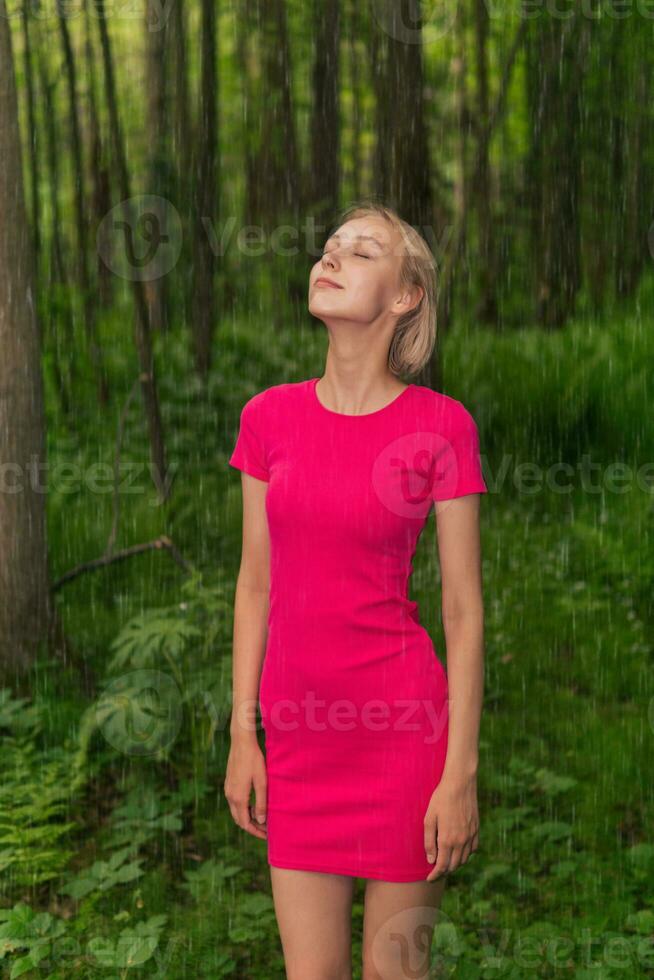 beautiful girl rejoices in the summer rain while walking in the forest photo