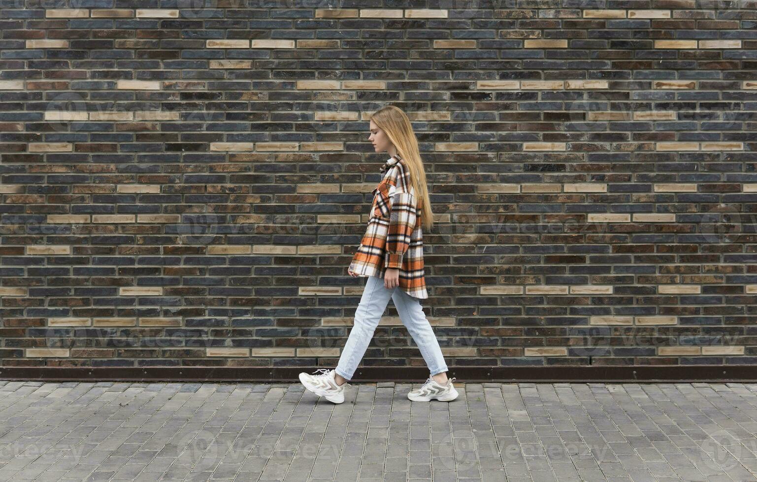 young woman walks down the street in front of a brick wall photo