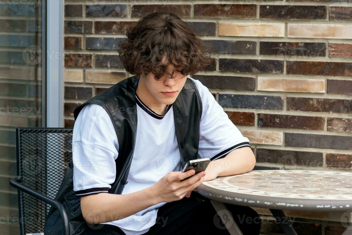 young man typing something on the phone while sitting at an outdoor cafeteria table photo